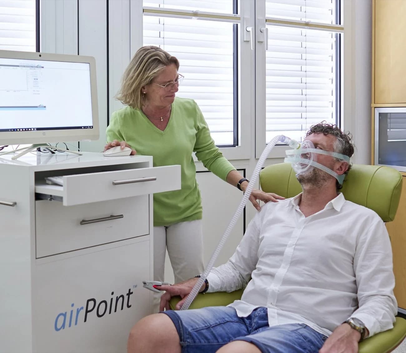 Ärztin betreut Patienten mit Atemmaske während einer Untersuchung am airPoint-Messgerät in einer medizinischen Praxis.