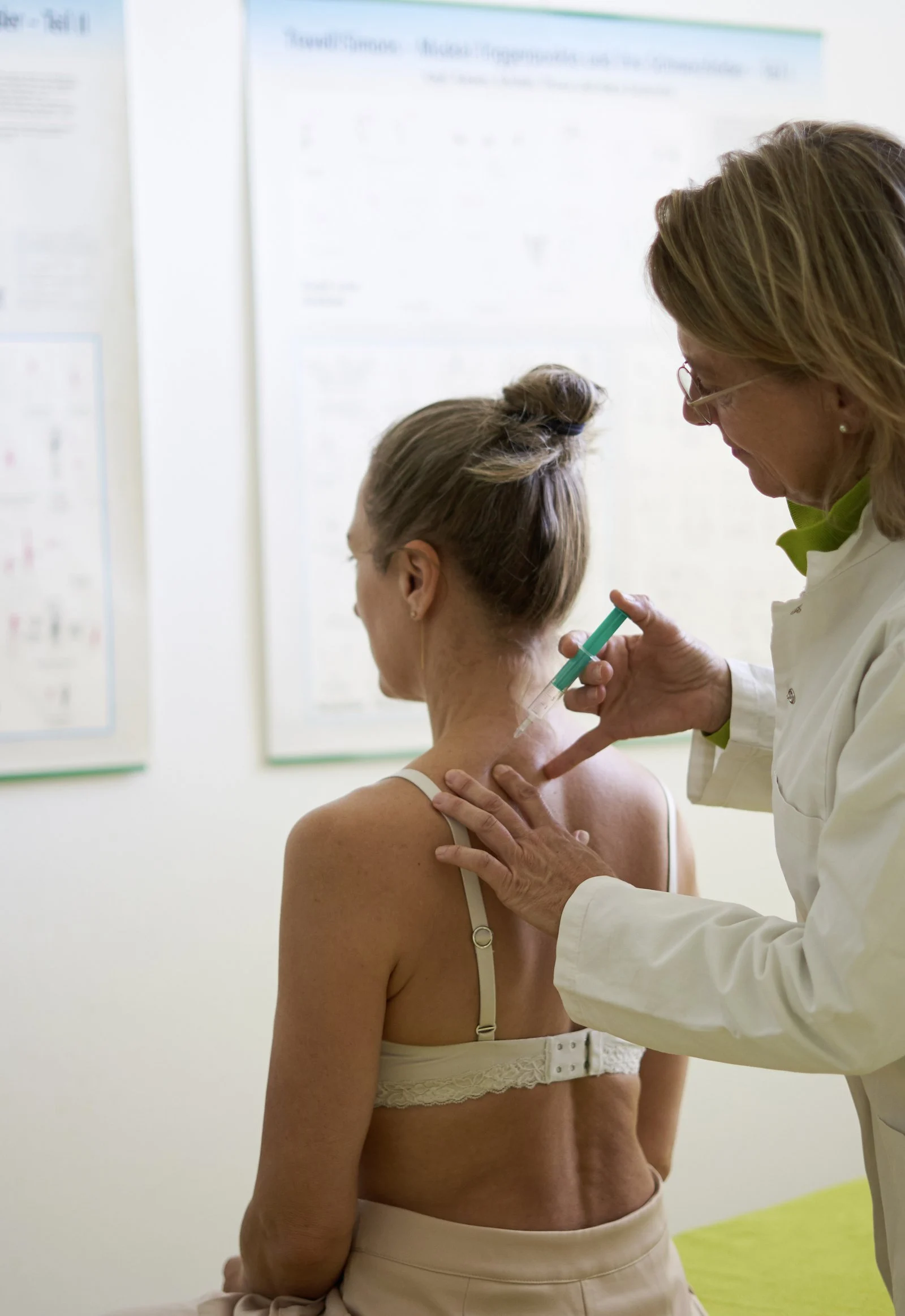 Ärztin setzt Patientin eine Spritze in den Nackenbereich vor medizinischen Lehrtafeln in einer Praxis.